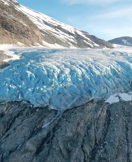 FPV drone flying over the blue ice of a glacier below a snowy mountain
